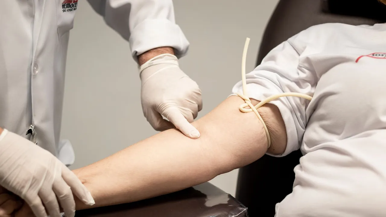 Medical professional wearing gloves preparing patient for blood draw using a tourniquet.