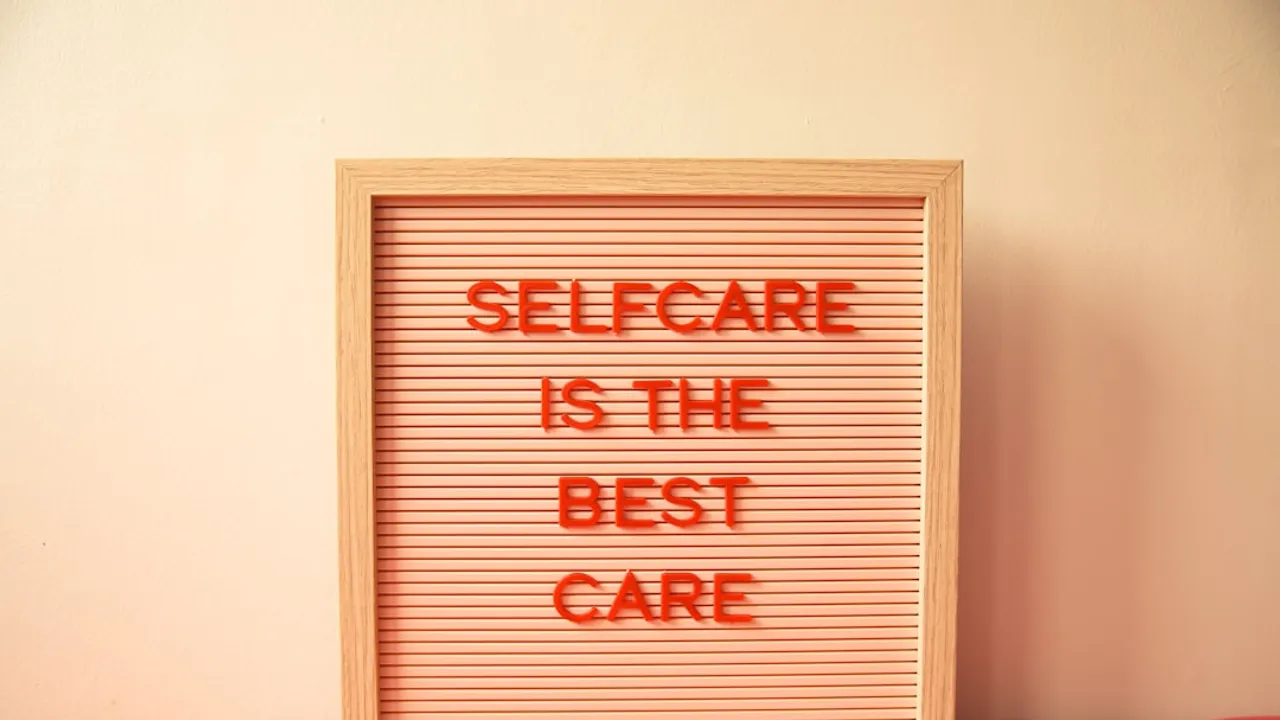 A wooden letter board with red text reading "SELFCARE IS THE BEST CARE"