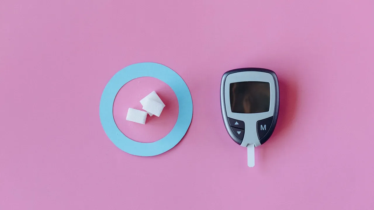 Flat lay of glucometer with sugar cubes on pink background, symbolizing diabetes awareness.